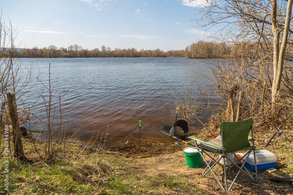 Obraz premium Place angler on the river Bank on a clear Sunny day in the spring. Fishing rods, fishing seat, tank, box of lures. The concept of active rest.