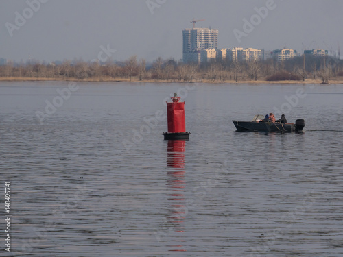 Wallpaper Mural fishermans in а motor boat and the red buoy for marking the channel on the river. Volga river, trees and city under construction multi-storey building. Saratov, Russia Torontodigital.ca