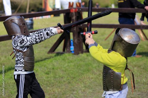 Dwóch chłopców w zbrojach rycerskich walczą na miecze.