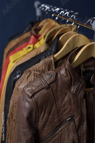 Many colored leather jacket hanging on rack on blue background