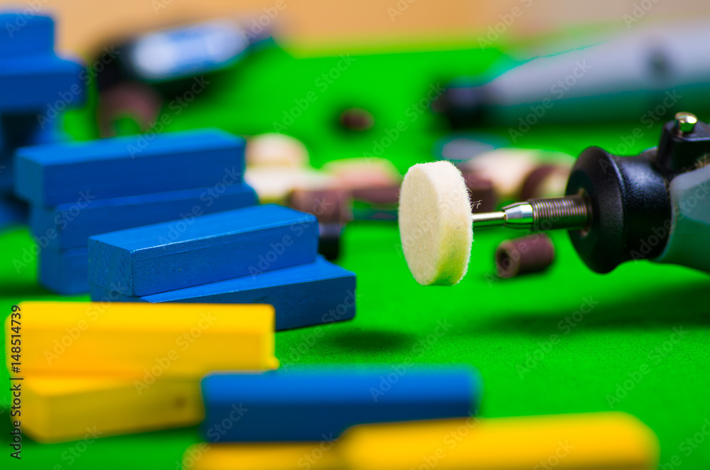 A closeup of gray drill with a small blue and yellow wooden pieces on a green background A closeup of gray drill with a small blue and yellow wooden pieces on a green background