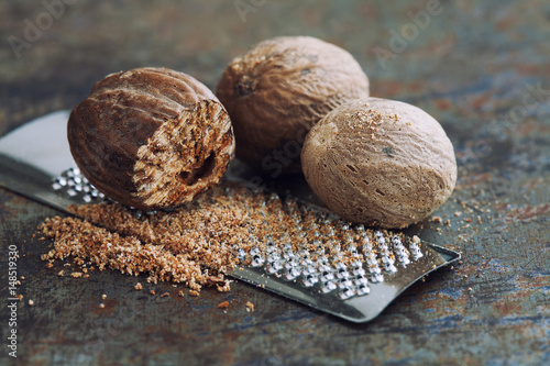 Making nutmeg powder. Macro view silver grater with grated muscat nuts. Kitchen still life photo. Shallow depth of field, retro rusty background. Selective focus.