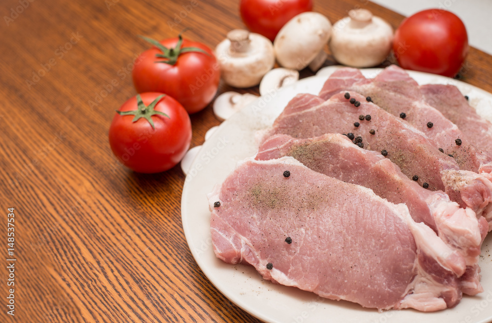 Slices of raw meat lie on a plate next to tomatoes and champignons Slices of raw meat lie on a plate next to tomatoes and champignons