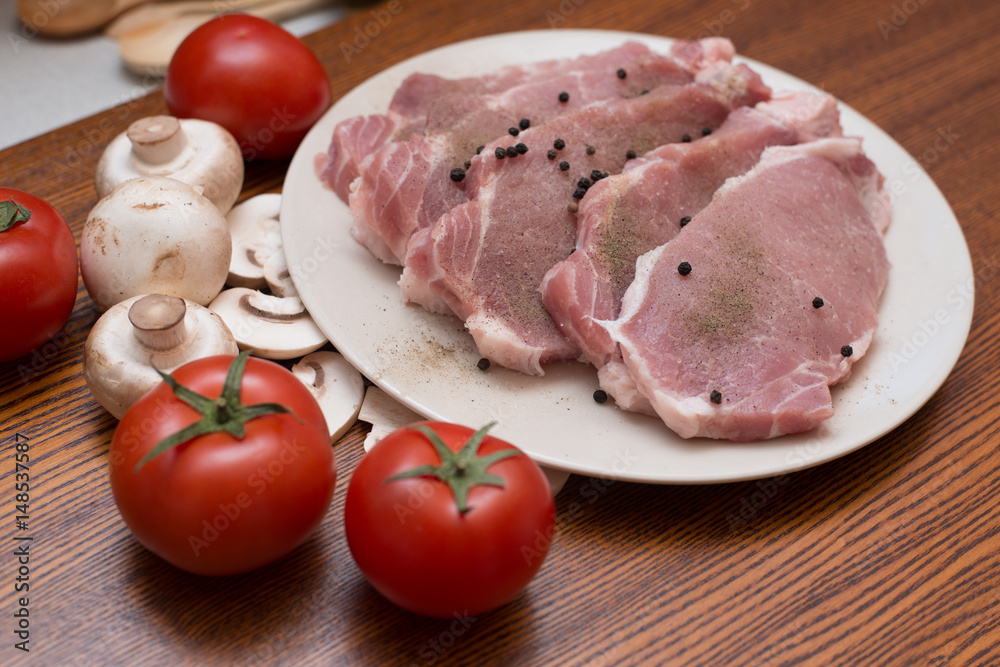 Slices of raw meat lie on a plate next to tomatoes and champignons Slices of raw meat lie on a plate next to tomatoes and champignons