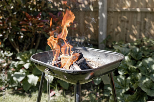 Preparing barbecue party in a garden. Burning charcoal with firestarter and wood.