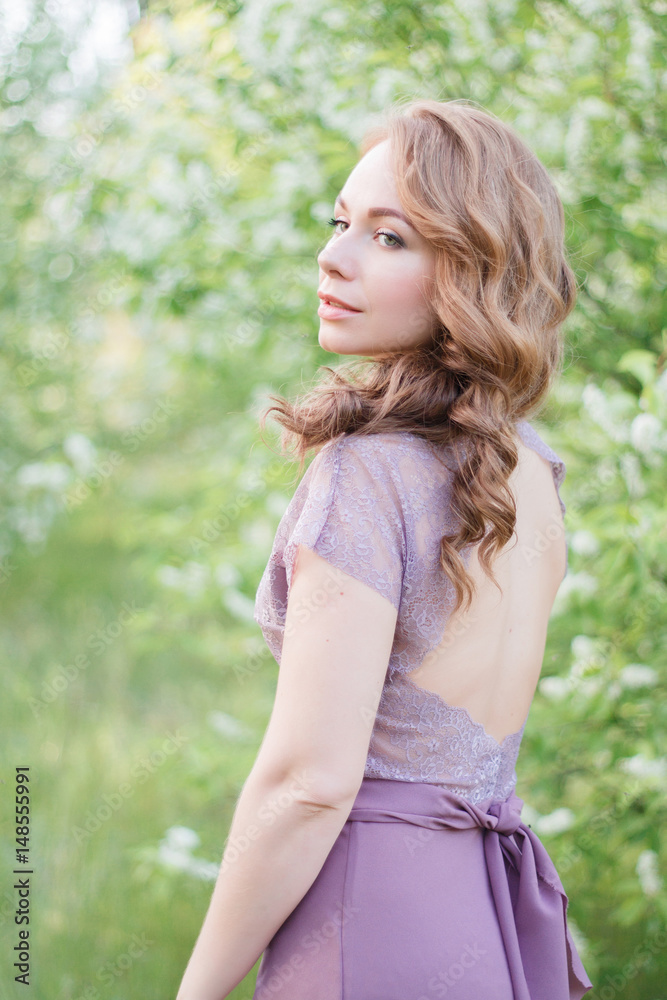 Beautiful young girl in a delicate tulle dress stands among the flowering spring trees in an outdoor park. Fine art