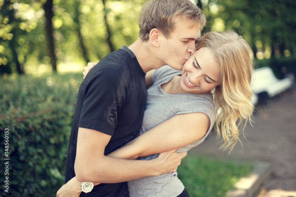 Happy young couple. Beautiful smiling blonde girl hugging her boyfriend in summer park.