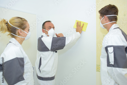 Man rubbing down wall, apprentices watching photo