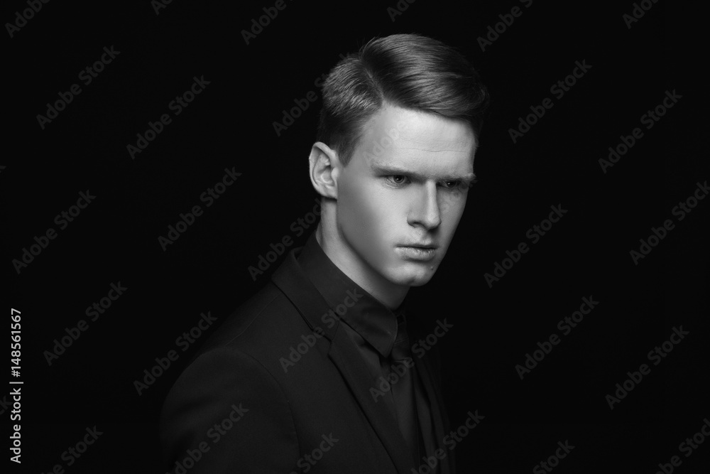 Fashion style studio portrait of young calm fashionable man in black costume on black backgound. Young male model with red hair