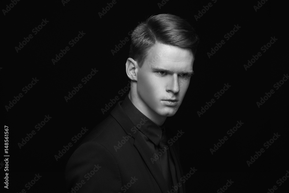 Fototapeta premium Fashion style studio portrait of young calm fashionable man in black costume on black backgound. Young male model with red hair