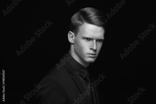 Fashion style studio portrait of young calm fashionable man in black costume on black backgound. Young male model with red hair