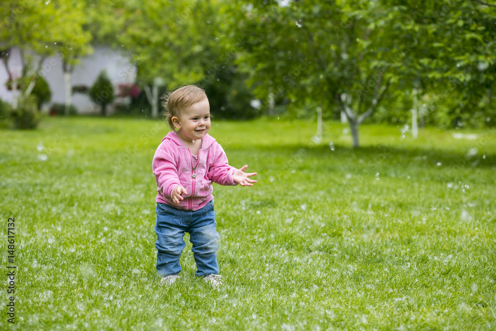 Little baby girl playing with poplar fluff on the green park outdoor. Little baby girl playing with poplar fluff on the green park outdoor.