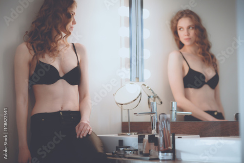 Young woman looking herself in the mirror on bathroom photo