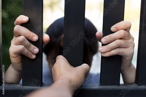 Asian teenager girl behind the metal bar with hand of visitor