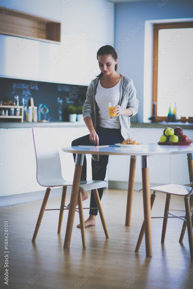 Young woman with orange juice and tablet in kitchen