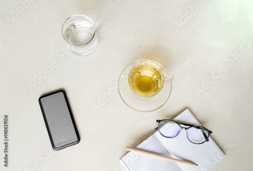Top view cup of tea with cell phone, glass of water and glasses with pencil