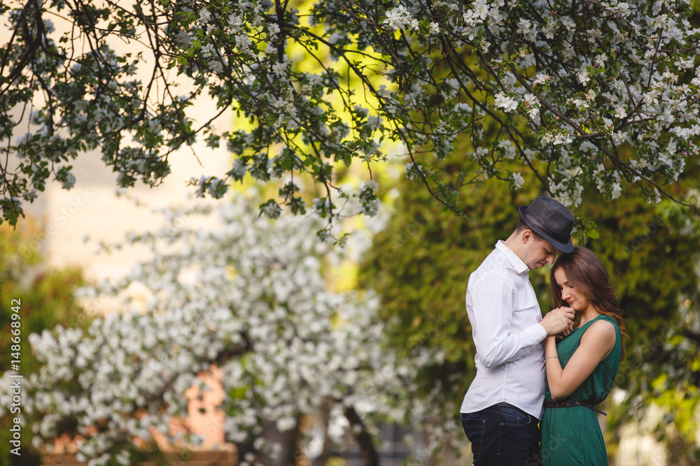 Young man and woman couple in a blooming apple garden. Tender holding each other. Spring lovestory. Brown-haired girl with long hairs. Young family Young man and woman couple in a blooming apple garden. Tender holding each other. Spring lovestory. Brown-haired girl with long hairs. Young family