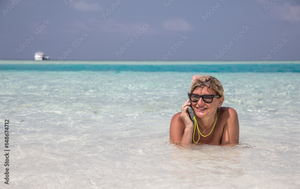 Girl is laying in blue waters of Indian ocean and speaking by telephone