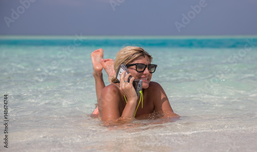 Beautiful smiling girl is laying in blue waters of Indian oceanand speaking by telephone