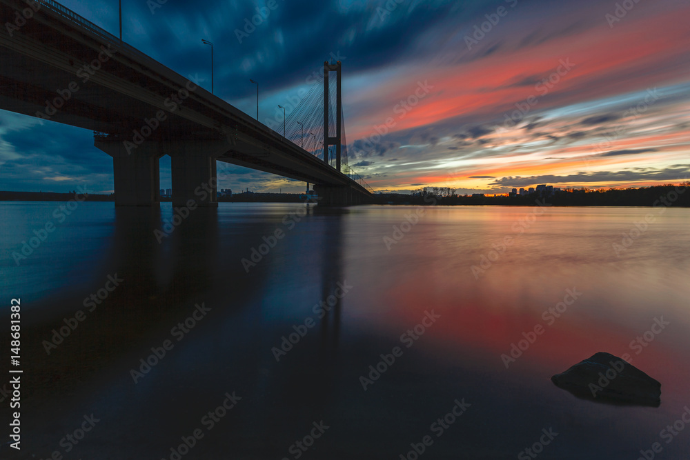Fototapeta premium Cityscape: sunset over the river against the bridge.