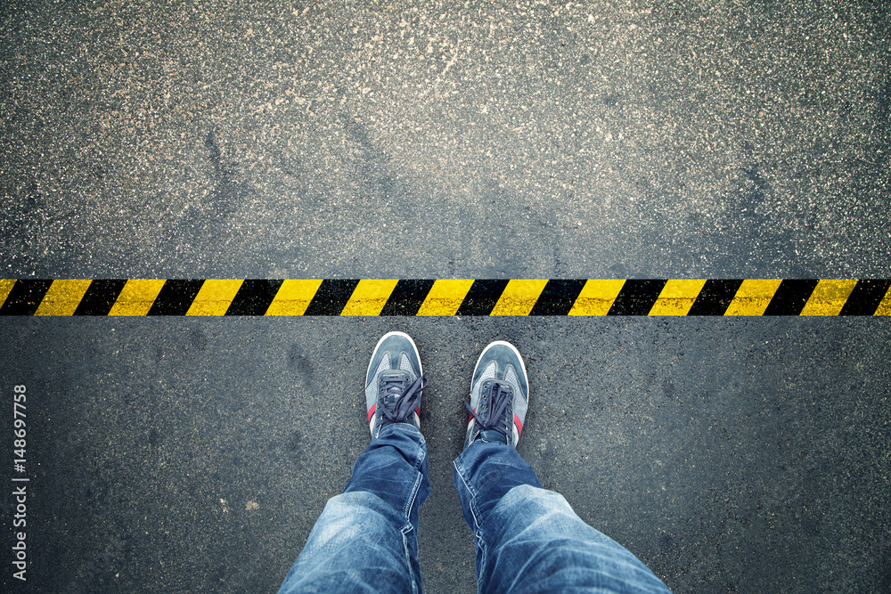 Top view of a man stands on industrial striped asphalt floor with warning yellow black pattern. - obrazy, fototapety, plakaty 