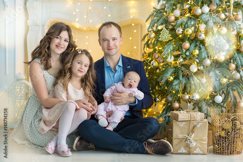 Family on Christmas eve at fireplace. Kids opening Xmas presents. Children under Christmas tree with gift boxes. Decorated living room with traditional fire place. Cozy warm winter evening at home.