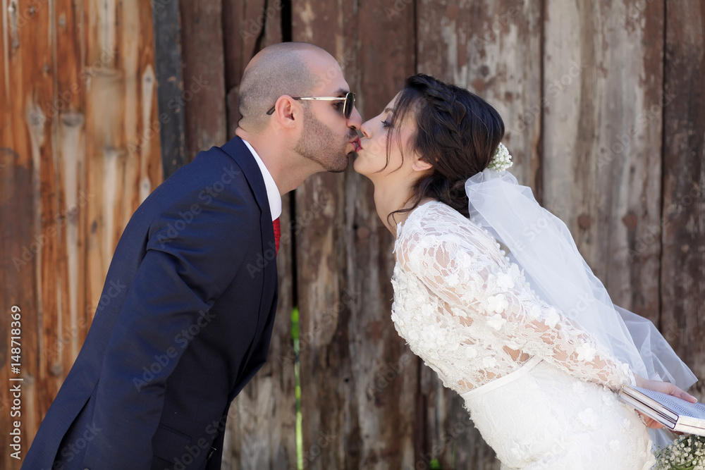 The bride in the groom kisses in front of the wooden fence