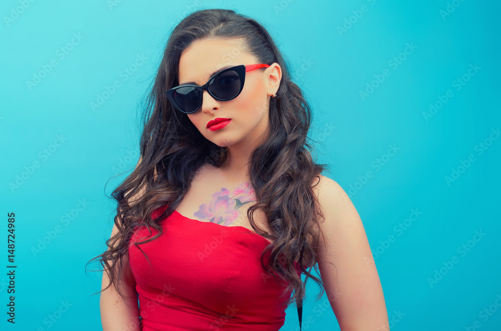 Portrait of the beautiful young woman in glasses on the red vintage dress on the blue background. Young female model. Portrait of the beautiful young woman in glasses on the red vintage dress on the blue background. Young female model.