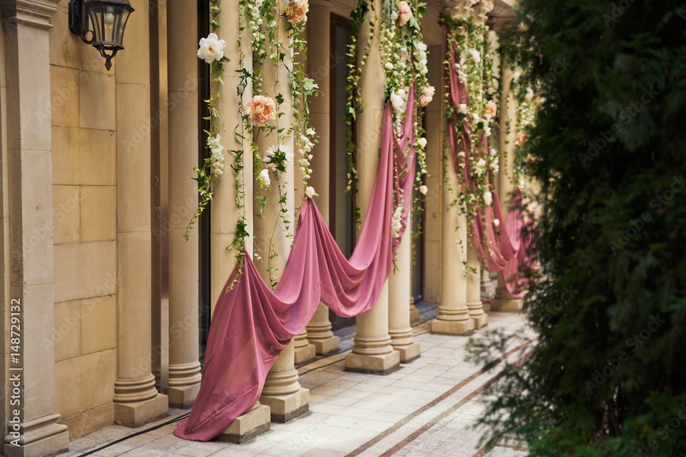 Beige pillars decorated with pink cloth and flower garlands Beige pillars decorated with pink cloth and flower garlands