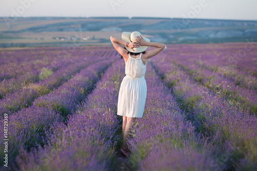 Young beautiful lady with lovely face walking on the lavender field on a weekend day in wonderful dresses and hats.