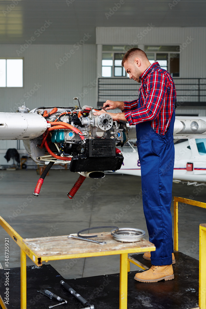 Airplane service crew working on preflight maintenance: young mechanic fixing turbine of jet plane in hangar Airplane service crew working on preflight maintenance: young mechanic fixing turbine of jet plane in hangar