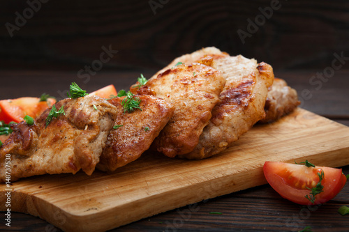 Sliced grilled pork barbecue meat on wooden cutting board over dark background