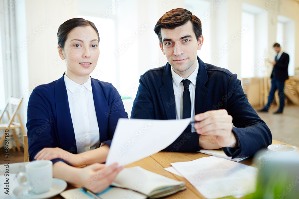 Young staff sitting by workplace and looking at camera Young staff sitting by workplace and looking at camera
