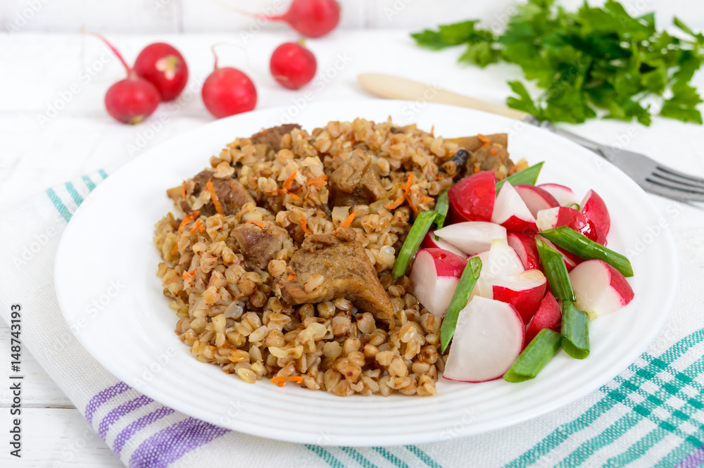 Buckwheat porridge with pieces of meat and a salad of radishes on a white wooden background.