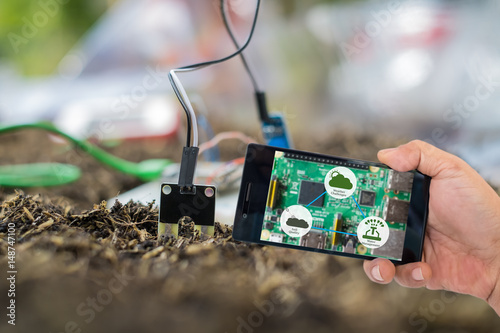 Agricultural technology and organic agriculture concept. Smart farmer holding smart phone with agritech icons and messages on screen with soil sensor to manage water, soil quality and monitor weather. photo