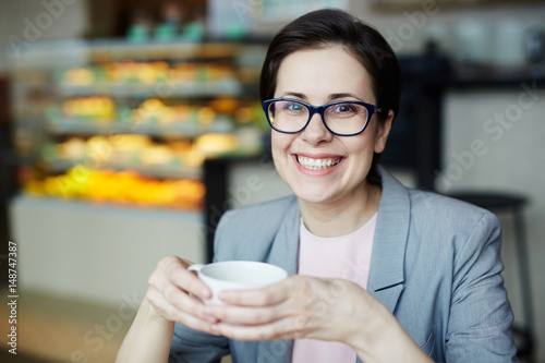 Happy businesswoman with cup of drink sitting in cafe