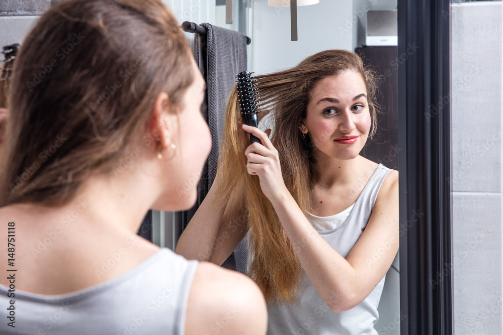 happy young woman brushing long hair in front of mirror happy young woman brushing long hair in front of mirror