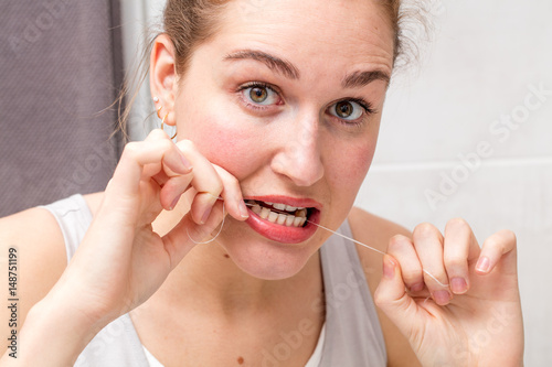 surprised young woman holding dental floss caring and cleaning teeth