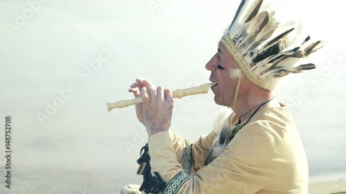 An Indian in a national costume plays a flute on the river bank 4k