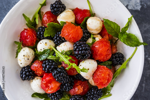 Delicious fruit salad with mozzarella in white plate on dark background.