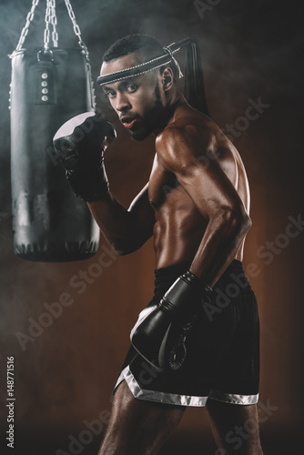 Side view of confident Muay Thai fighter with punching bag behind © LIGHTFIELD STUDIOS