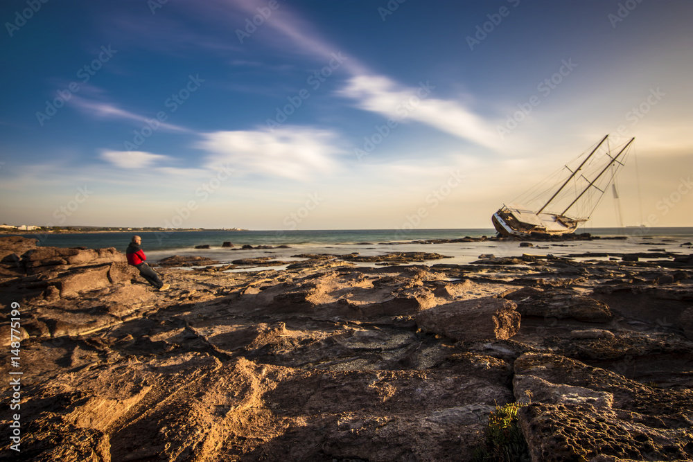A man look the shipwrecked Boat in Calasetta, on the coast of south Sardinia where is sitting even today