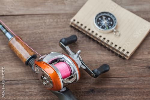 Fishing tackle - Baitcasting Reel, book and compass on wooden background