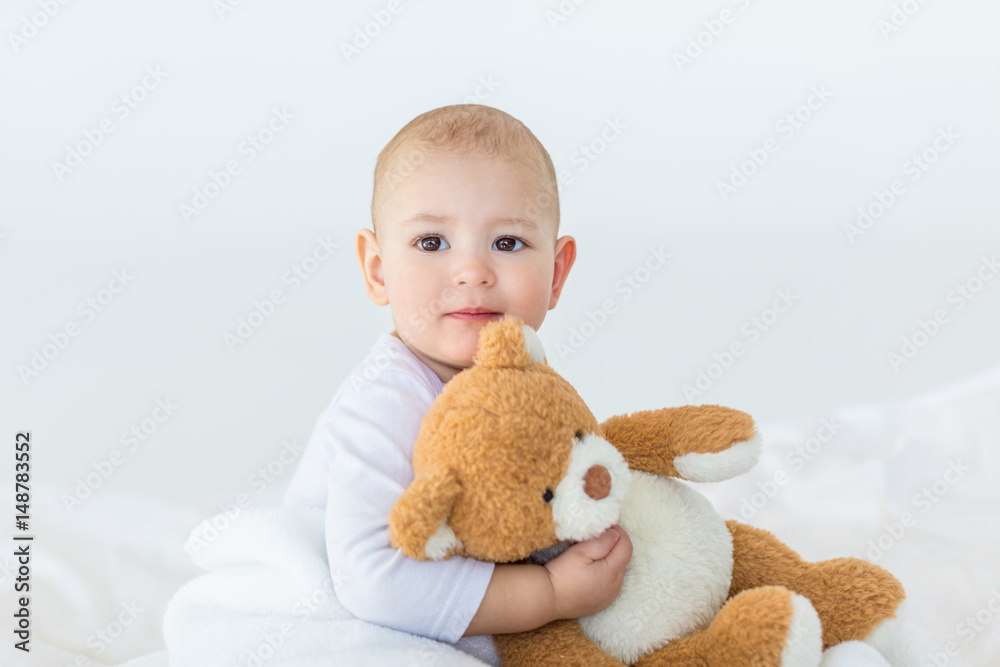 Portrait of adorable small baby boy with teddy bear playing on bed, 1 year old baby concept