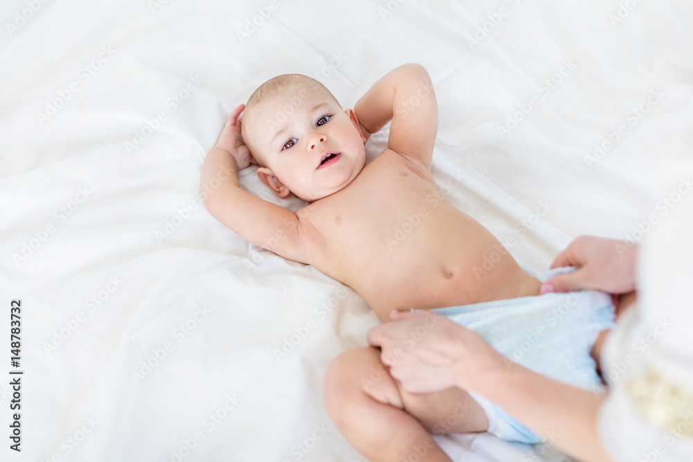Cropped shot of mother changing diaper of adorable baby boy lying on bed, 1 year old baby concept