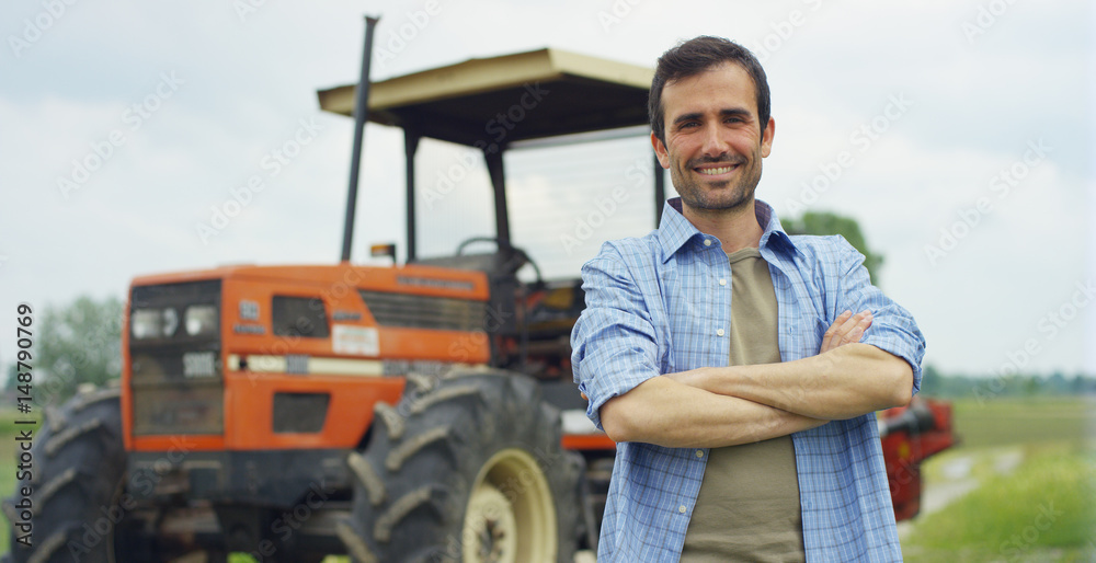 Portrait of a handsome young farmer standing in a shirt and smiling at the camera, on a tractor and nature background. Concept: bio ecology, clean environment, beautiful and healthy people, farmers.