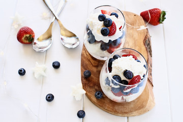 Trifles made with blueberries, strawberries, whipped cream and star shaped pound cake against a white wood background. Perfect for fourth of July. Shallow depth of field with selective focus.