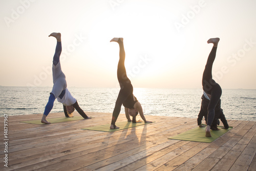 one man and two womans make yoga training in the morning on the beach