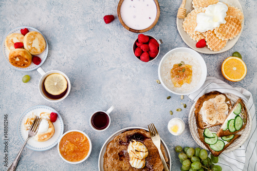 Morning atmosphere. Healthy breakfast with porridge, oatmeal, pancakes, lots of berries and snacks on blue rustic background. Text space at the center.