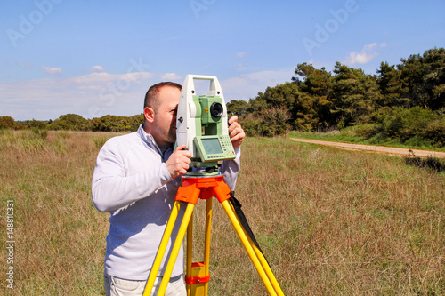 Man using of total station. Guy surveyor at work. Survey Instrument geodetic device, total station set and surveyor worker making measurement in the field. Total station outdoor at construction site.